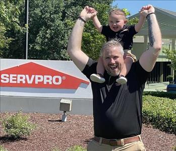 A Servpro owner stands by a Servpro sign with his daughter on his shoulders.